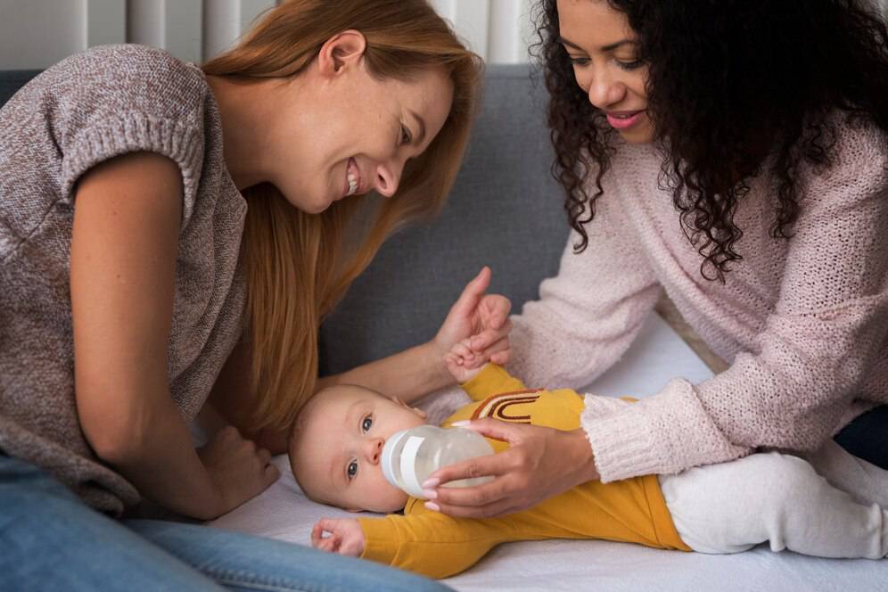 A mother using a breast pump while holding her sleeping baby in a nursery.
