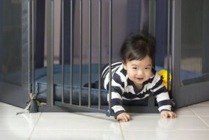 A joyful toddler crawling through a safety gate, smiling brightly, dressed in a striped outfit.
