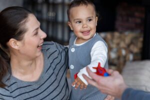 A joyful woman playing with a smiling toddler reaching for a toy airplane.
