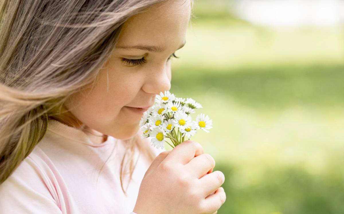 Young girl smelling a bouquet of daisies outdoors in a sunny park.