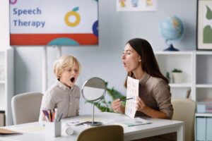 A speech therapist and a young boy practicing vocal exercises in a colorful therapy room.