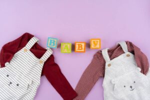 Two baby outfits and blocks spelling "BABY" on a purple background.