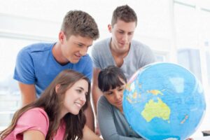 Four young people gather around a large globe, pointing and examining locations.