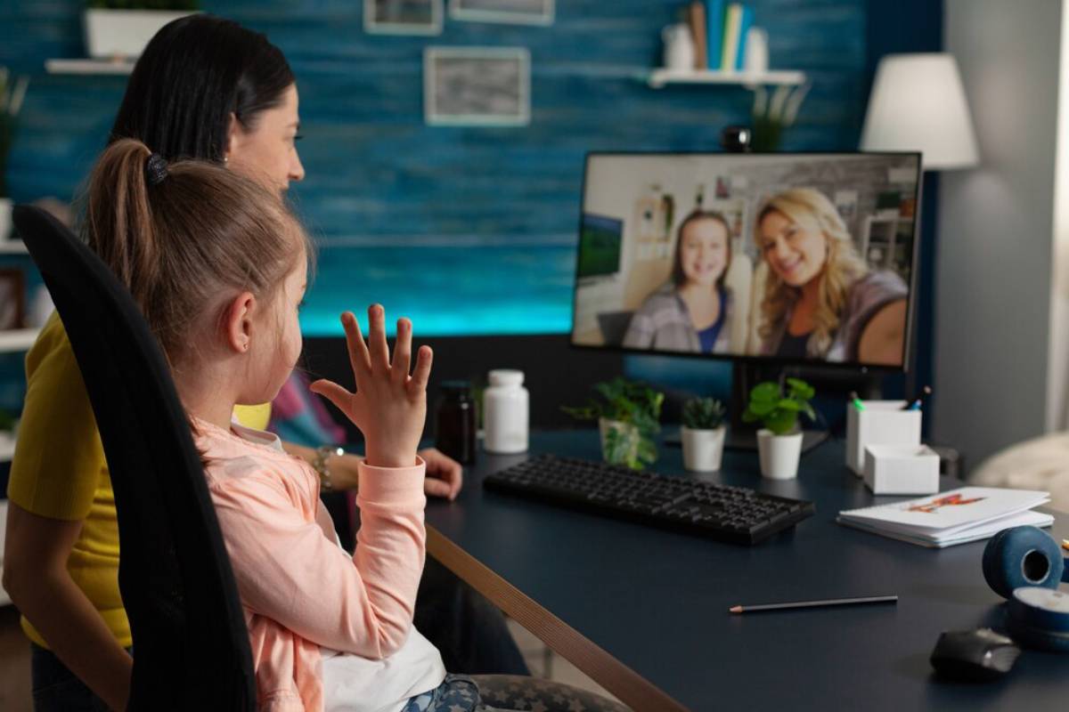 Woman and child in a home office, video chatting with another woman and child on a computer screen.