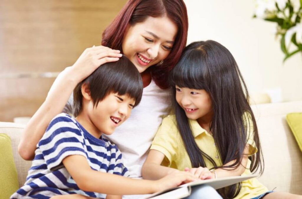 A joyful mother with her son and daughter looking at a tablet and smiling in a living room.