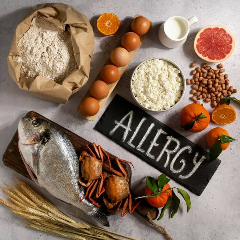 Various common allergenic foods like nuts, eggs, milk, wheat, fish, and shellfish displayed around a sign labeled 