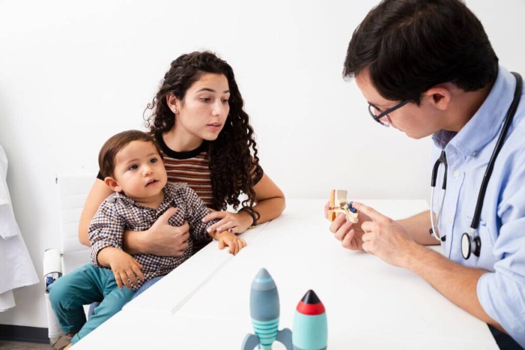 A pediatrician showing a toy to a young child and mother during an examination.