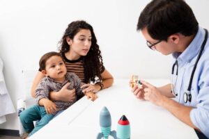 A pediatrician showing a toy to a young child and mother during an examination.