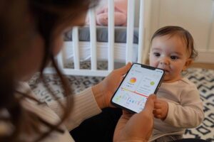 Woman showing a smartphone with colorful graphs to a curious baby indoors.