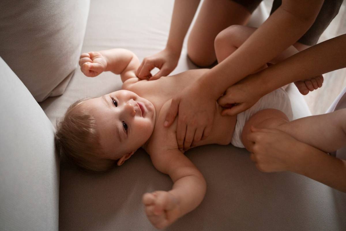 A baby lying on a couch with another child touching its belly gently.